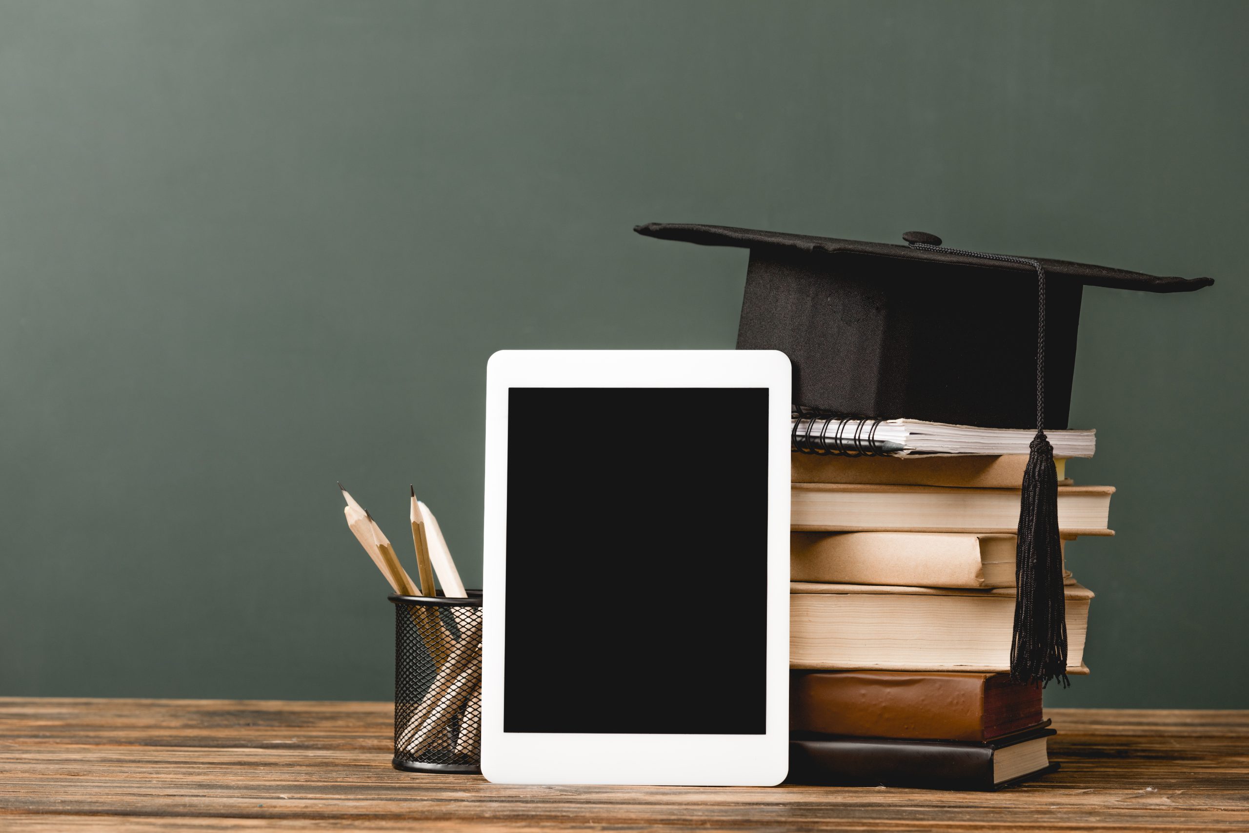 books, notebook, academic cap and digital tablet with blank screen on wooden surface isolated on
